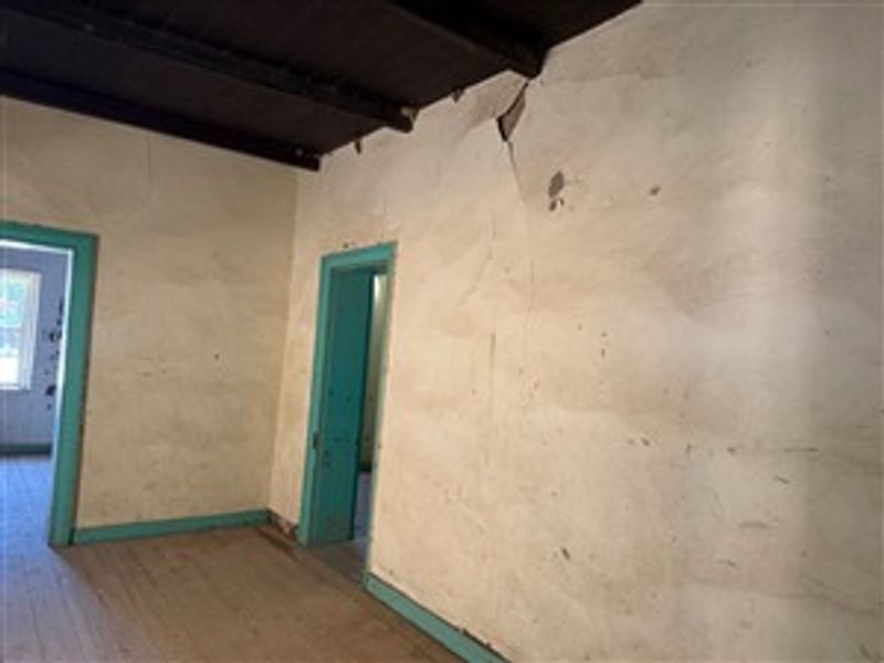 An empty living room featuring exposed timber ceiling beams, timber flooring, and significant wall plaster cracking requiring repair and cosmetic refurbishment.
