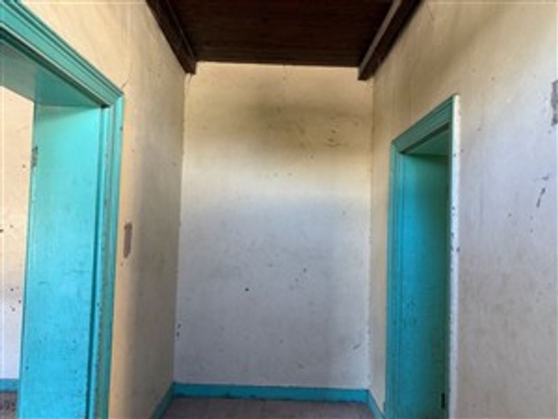 A vacant interior hallway featuring a timber ceiling and painted door frames, requiring significant cosmetic refurbishment and wall repairs.