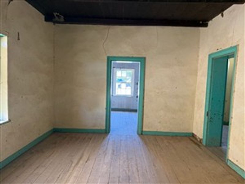 An empty living room featuring original timber flooring, exposed ceiling beams, and dated wall finishes, offering a blank canvas for renovation.