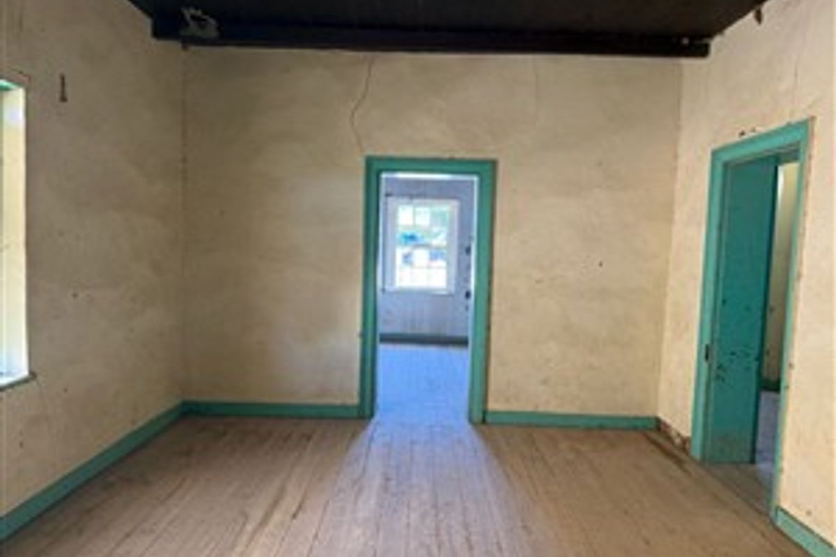 An empty living room featuring original timber flooring, exposed ceiling beams, and dated wall finishes, offering a blank canvas for renovation.