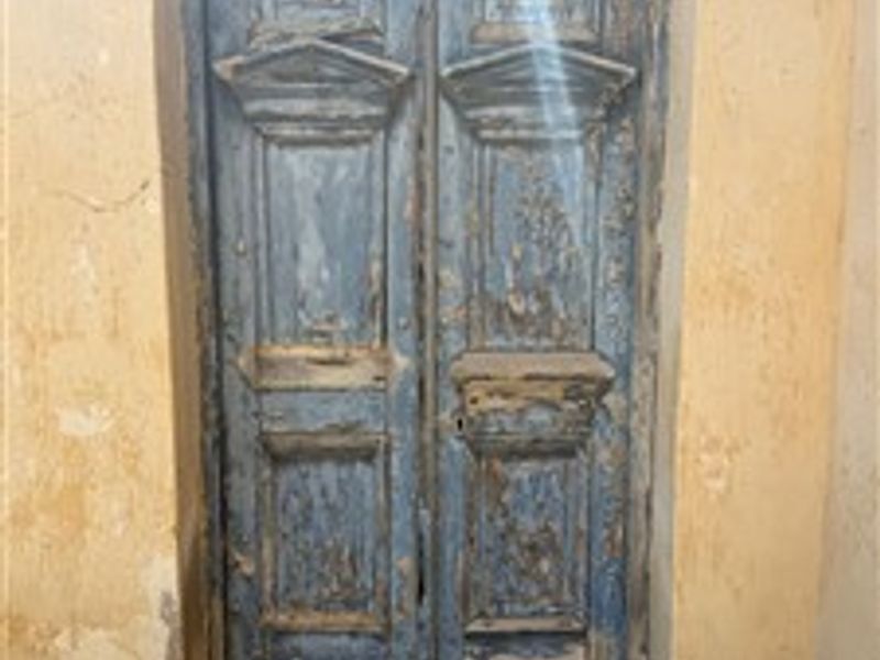 A weathered timber double door set within a rustic plaster wall, showing significant signs of age and wear.