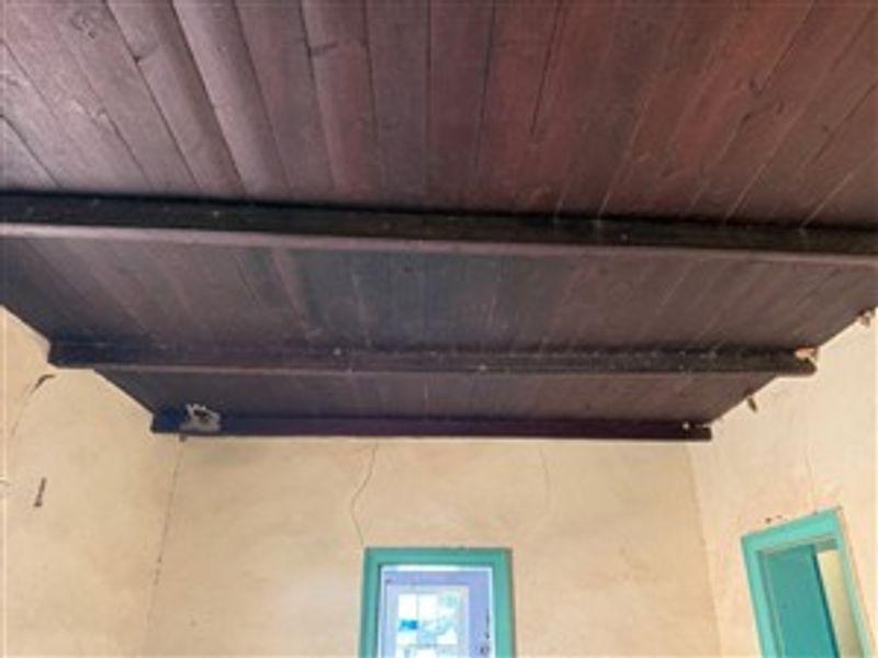Interior space featuring exposed timber ceiling beams and plank ceiling, showing significant wall cracking and signs of wear requiring maintenance.