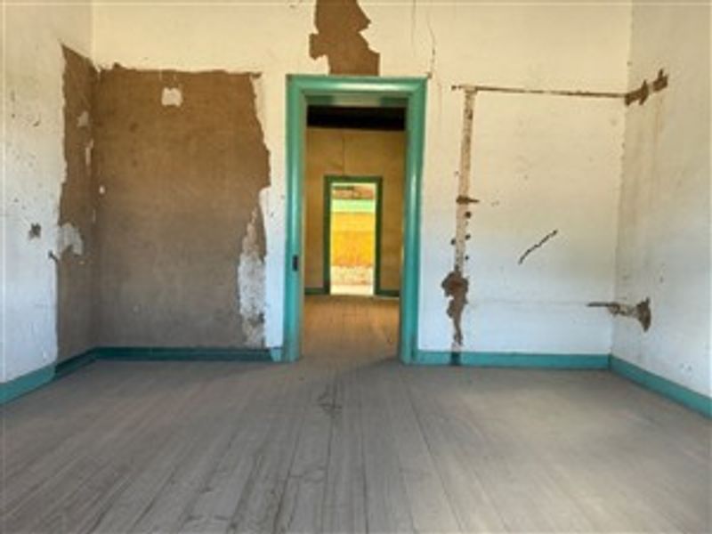 An empty room in need of significant renovation, featuring original timber flooring and damaged wall plaster throughout the interior space.