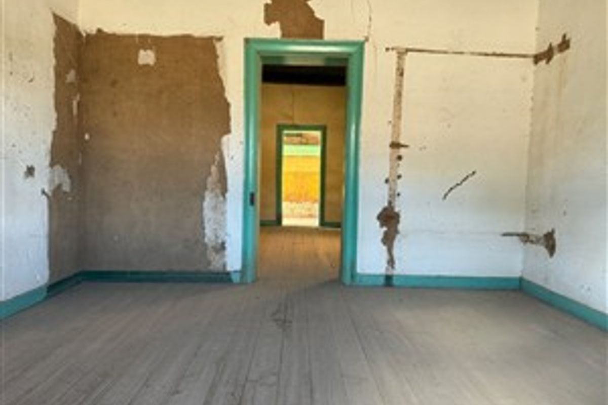 An empty room in need of significant renovation, featuring original timber flooring and damaged wall plaster throughout the interior space.