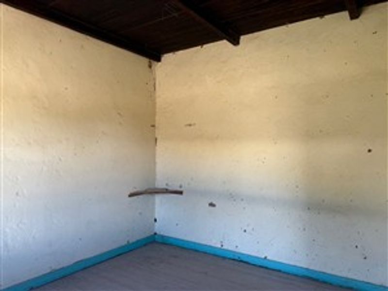 An empty room featuring exposed timber ceiling beams and a corner shelf, requiring cosmetic updates to the wall finishes.