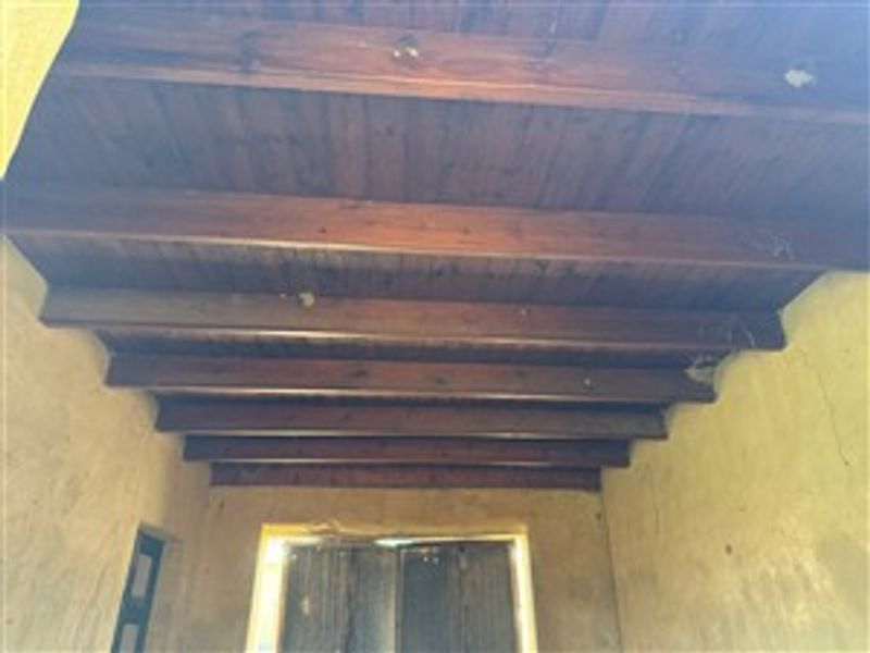An entrance area featuring exposed timber ceiling beams and a rustic timber door, showing signs of wear and requiring cosmetic attention.