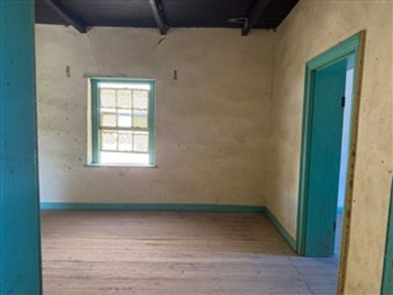 An empty bedroom featuring exposed timber ceiling beams, original timber sash windows, and timber flooring, requiring cosmetic renovation and wall repairs.