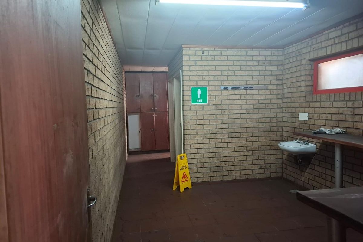 A functional commercial restroom facility featuring exposed brick walls, built-in lockers, a wall-mounted basin, and tiled flooring.