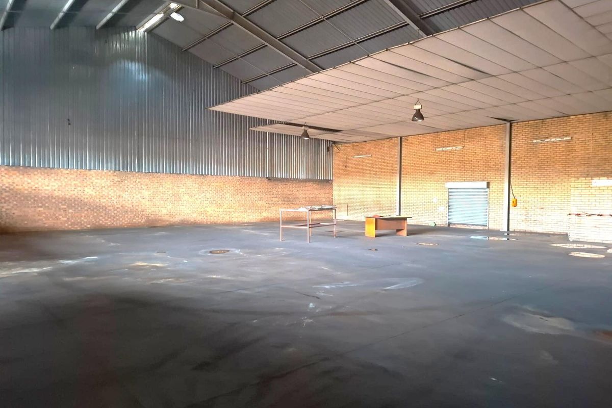 Spacious commercial warehouse featuring high-volume ceilings, exposed brick walls, and durable concrete flooring, suitable for various industrial or storage applications.