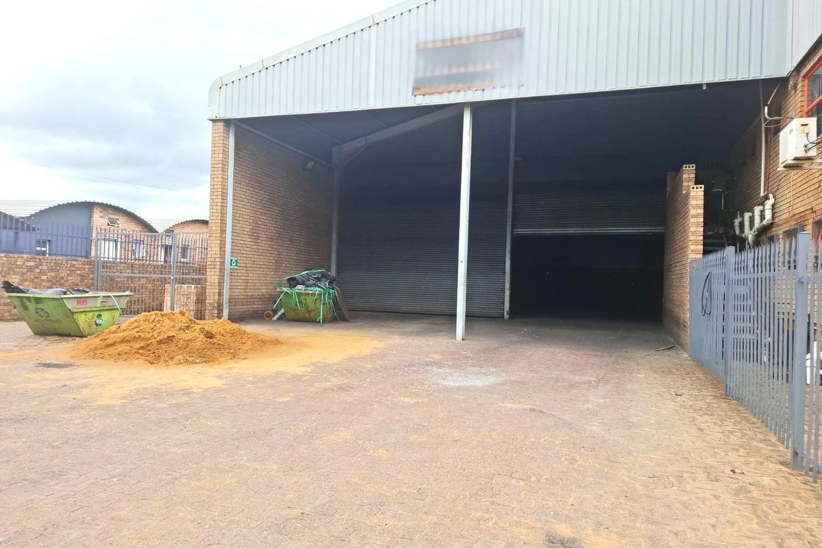 Commercial warehouse exterior featuring a large roller shutter door, brick facade, and paved yard area suitable for industrial or storage use.