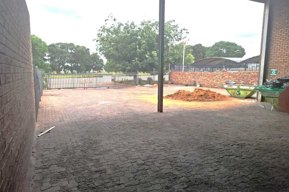 A covered commercial outdoor area featuring brick paving, perimeter brick walls, and a metal security gate, providing functional access to the property exterior.