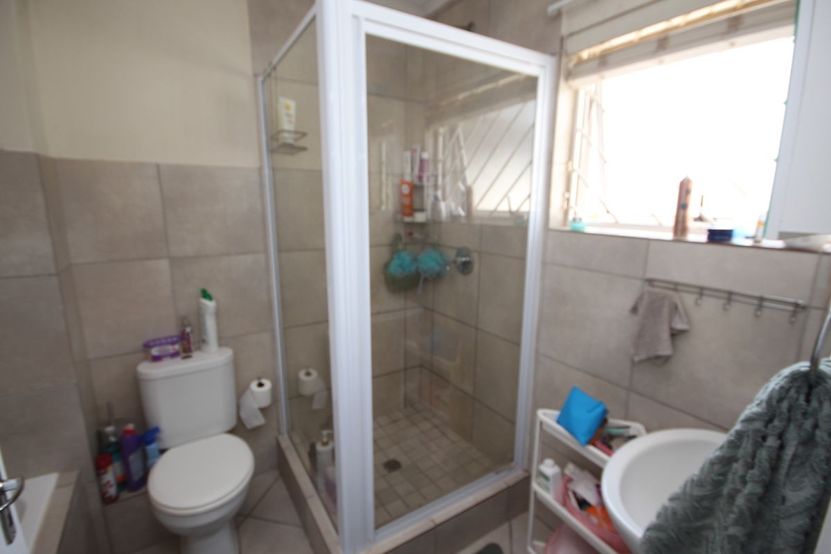 A functional bathroom featuring a glass-enclosed shower, a standard toilet, and a wall-mounted basin with neutral wall and floor tiling.