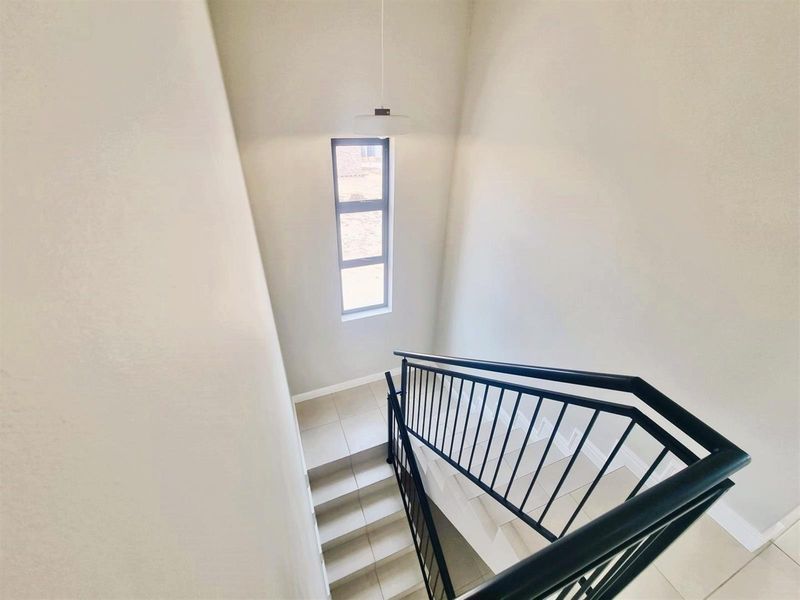 A bright and modern staircase featuring tiled steps, a sleek black metal balustrade, and a tall vertical window providing natural light.