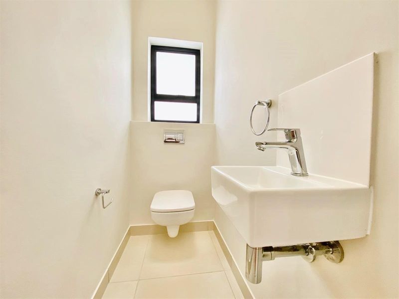 A clean, modern guest bathroom featuring a wall-mounted toilet, a compact wall-mounted basin with a chrome mixer tap, and neutral floor tiles.