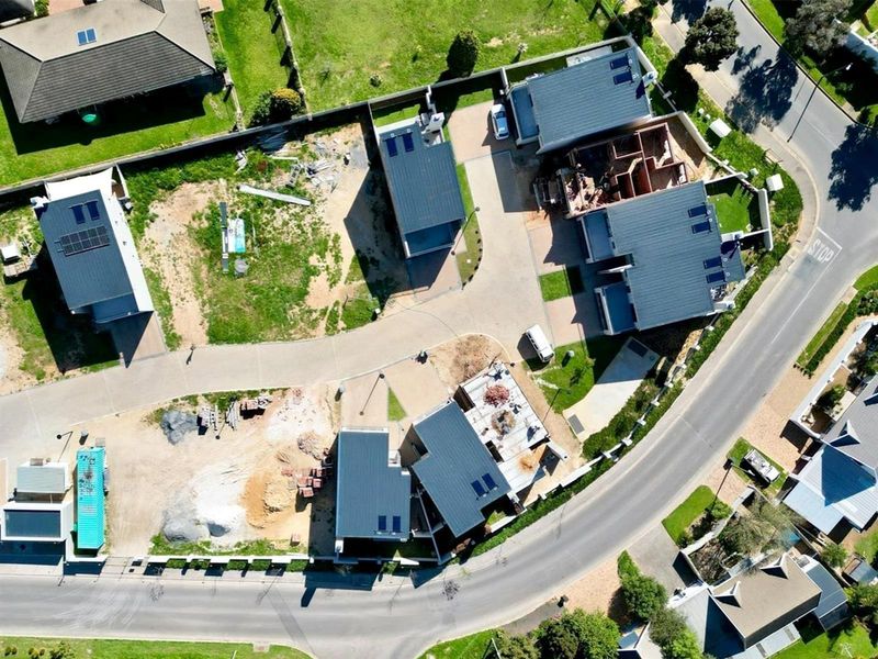 Aerial view of a residential development site showing multiple houses in various stages of construction with paved access roads and boundary fencing.