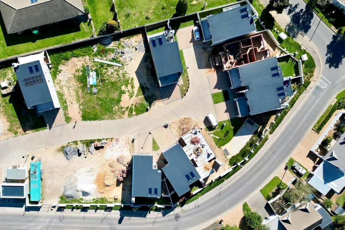 Aerial view of a residential development site showing multiple houses in various stages of construction with paved access roads and boundary fencing.