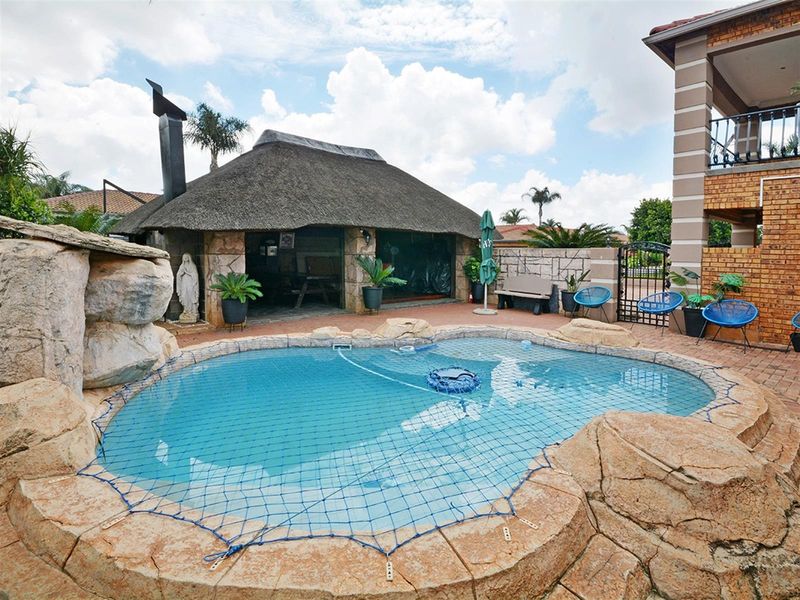 Outdoor entertainment area featuring a swimming pool with rock-style coping and a thatched lapa structure with a built-in fireplace.