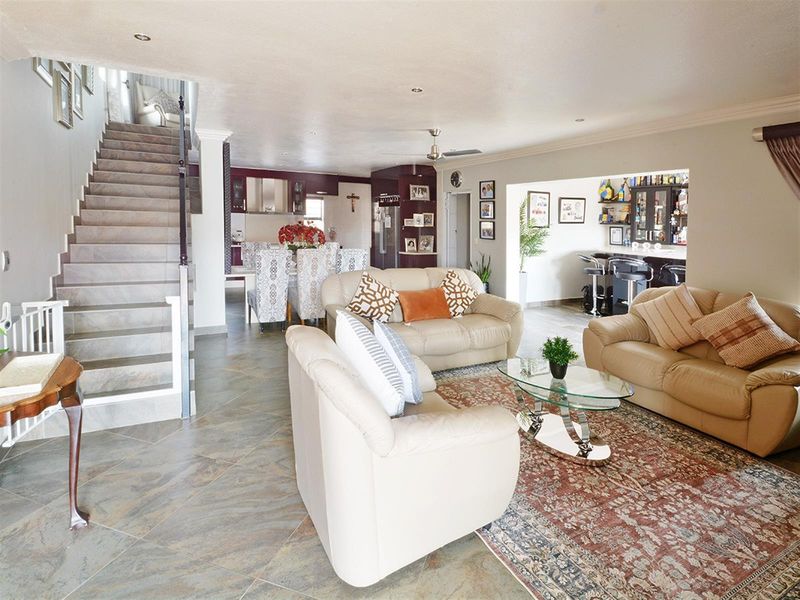 Open-plan living area featuring tiled flooring, a staircase with metal balustrades, and a connected kitchen and bar area.