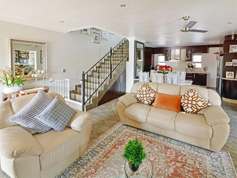 Open plan living area featuring a staircase with wrought iron railing, tiled flooring, and a modern kitchen with dark cabinetry in the background.