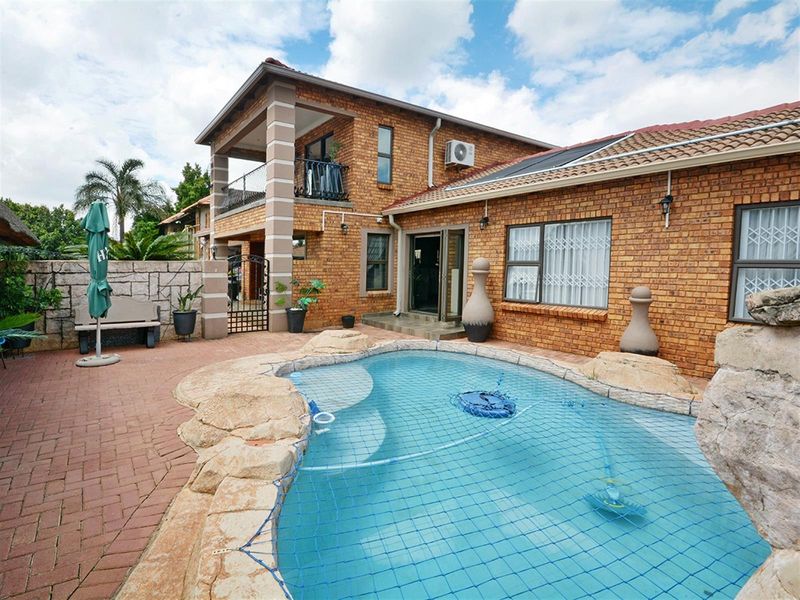 Rear exterior view featuring a brick-faced two-story house, a swimming pool with safety net, and a paved patio area.