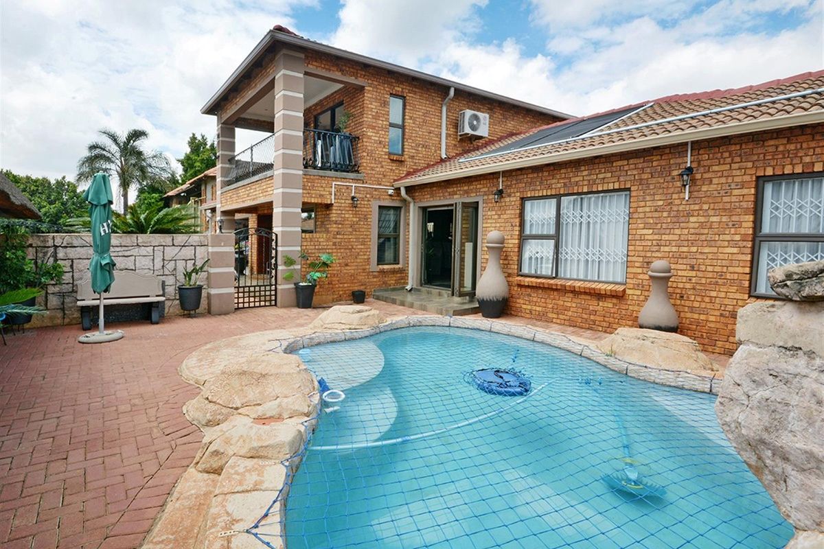 Rear exterior view featuring a brick-faced two-story house, a swimming pool with safety net, and a paved patio area.