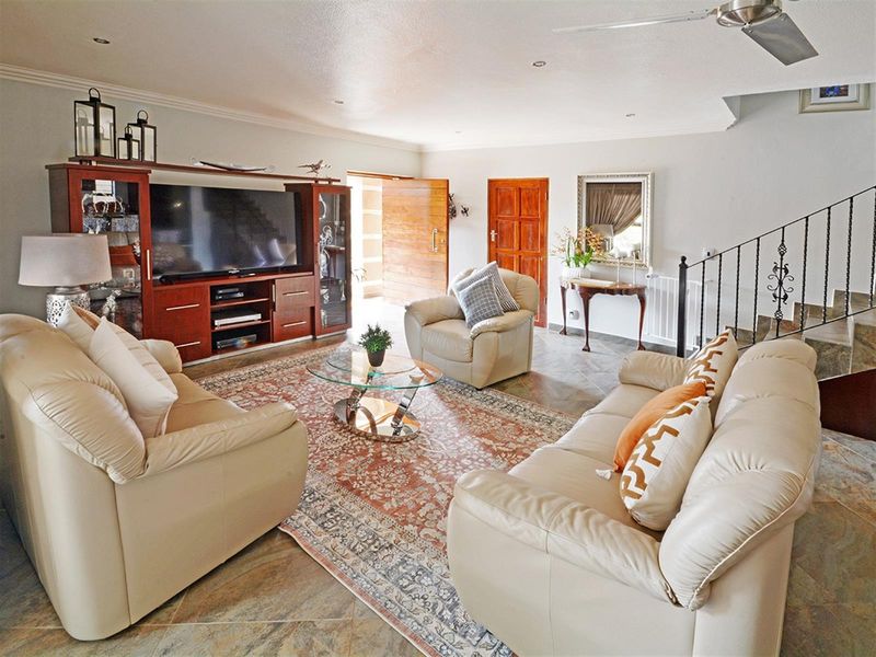 Spacious living room featuring tiled flooring, recessed ceiling lighting, a ceiling fan, and a staircase with decorative wrought iron railings.