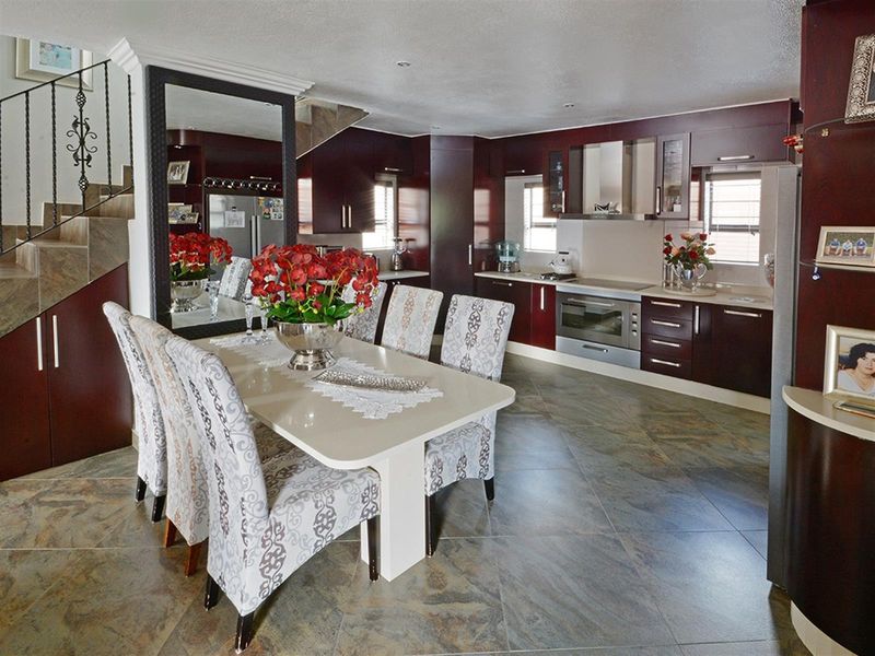 Open-plan kitchen and dining area featuring dark wood cabinetry, built-in oven, extractor fan, and tiled flooring, adjacent to a staircase.