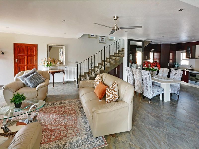 Spacious open-plan living and dining area featuring tiled flooring, a central staircase with wrought iron railing, and a modern kitchen with dark cabinetry.