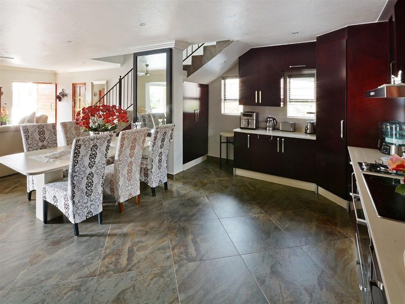 Open-plan kitchen and dining area featuring dark cabinetry, stone-look floor tiles, and a staircase with a decorative metal balustrade.