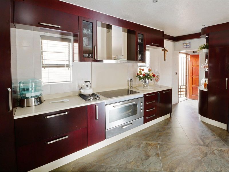 A well-maintained kitchen featuring dark wood cabinetry, stone countertops, a built-in oven, and a modern extractor fan with tiled flooring.