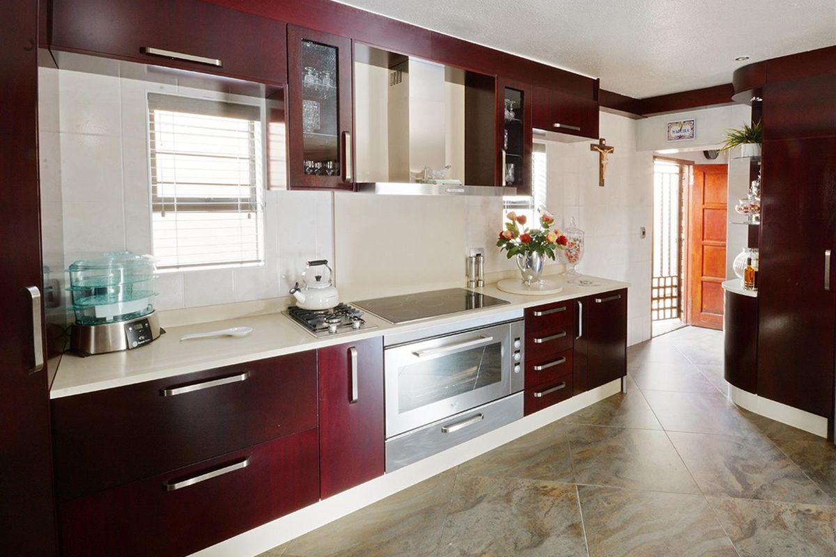 A well-maintained kitchen featuring dark wood cabinetry, stone countertops, a built-in oven, and a modern extractor fan with tiled flooring.