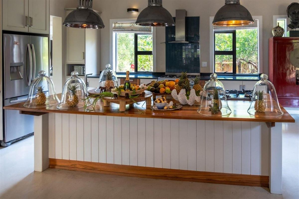 Spacious kitchen featuring a large wooden island, modern cabinetry, stainless steel appliances, and industrial-style pendant lighting with views of the garden.