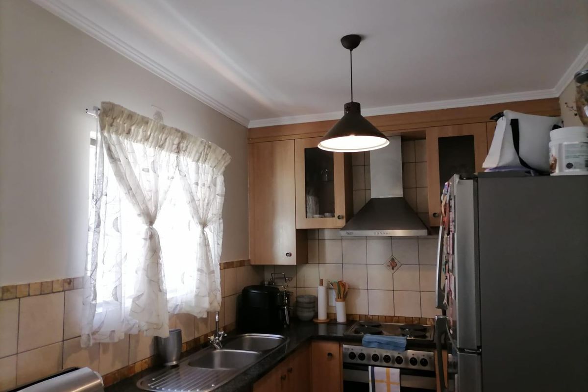 A functional kitchen featuring wooden cabinetry, granite countertops, a stainless steel gas hob with extractor fan, and tiled backsplash.