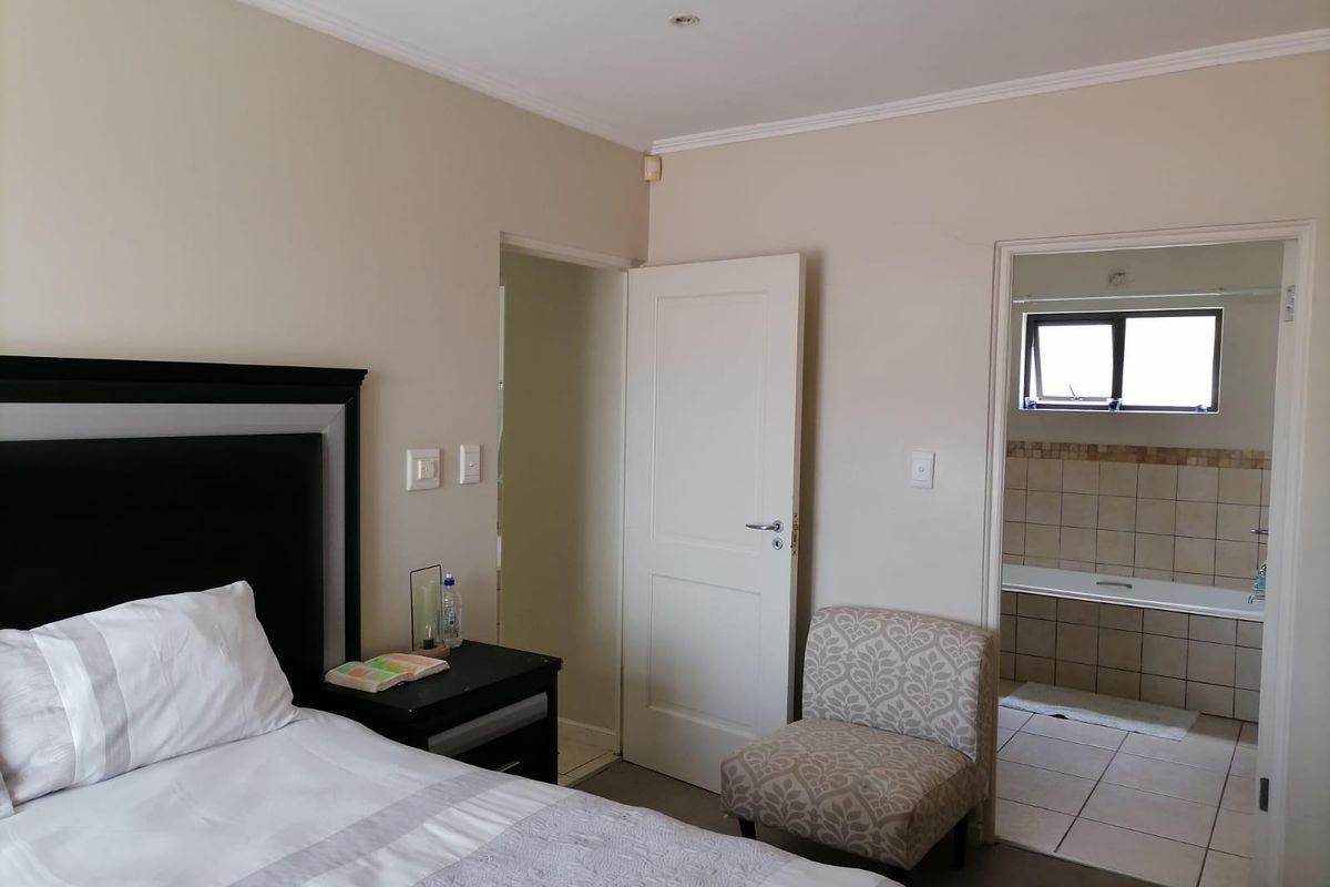 A well-maintained bedroom featuring an en-suite bathroom with a built-in bathtub, neutral wall tones, and recessed ceiling lighting.