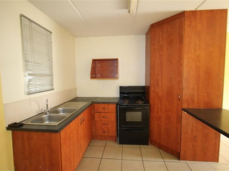 A functional kitchen featuring laminate cabinetry, a double bowl stainless steel sink, a freestanding stove, and tiled flooring.