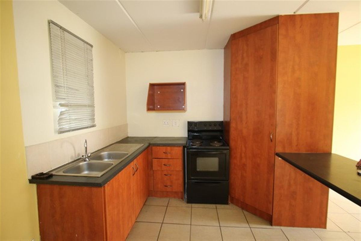 A functional kitchen featuring laminate cabinetry, a double bowl stainless steel sink, a freestanding stove, and tiled flooring.