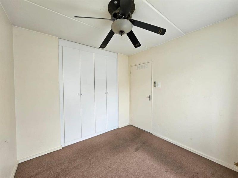An empty bedroom featuring built-in cupboards, a ceiling fan, and carpeted flooring, requiring cosmetic updates to improve its overall condition.