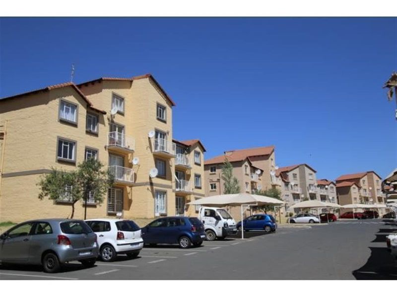 Exterior view of a multi-story townhouse complex featuring yellow facade, tiled roofs, private balconies, and dedicated covered parking bays.