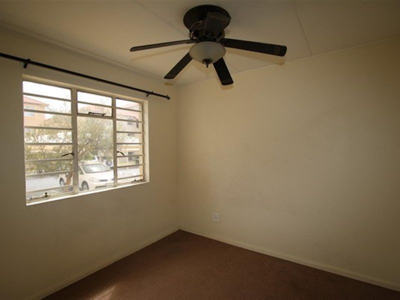 An empty bedroom featuring a ceiling fan, carpeted flooring, and a metal-framed window with natural light.