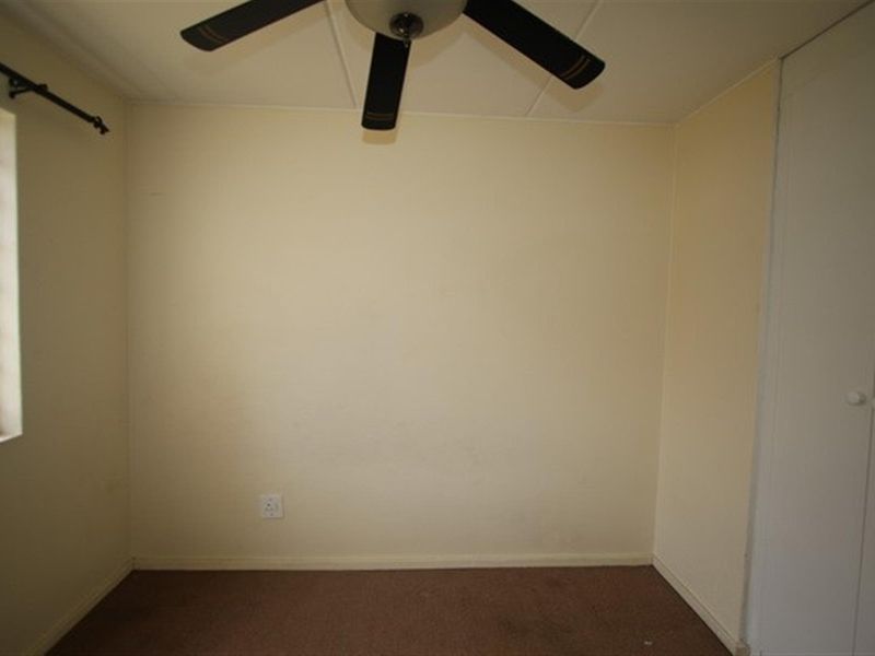 An empty bedroom featuring a ceiling fan, built-in cupboard storage, and security bars on the window.