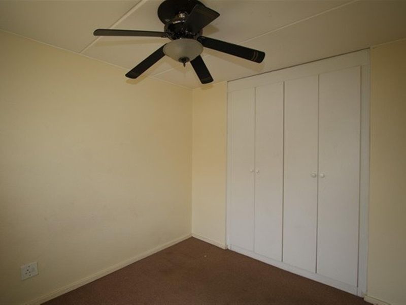 An empty bedroom featuring a ceiling fan, built-in wardrobe, and carpet flooring, offering a blank canvas for personalization.