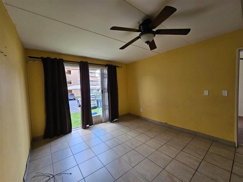 An empty living room featuring tiled flooring, a ceiling fan, and a sliding glass door with security gate leading to the exterior.