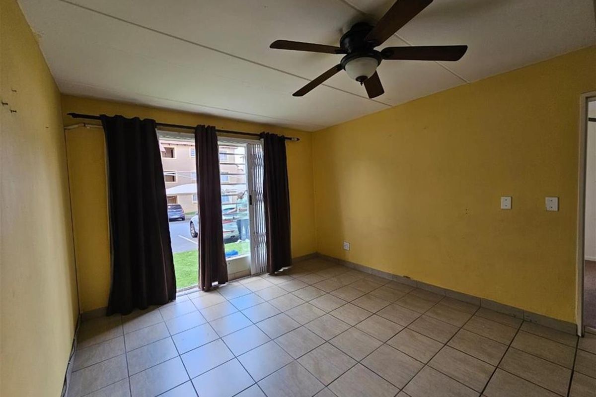 An empty living room featuring tiled flooring, a ceiling fan, and a sliding glass door with security gate leading to the exterior.