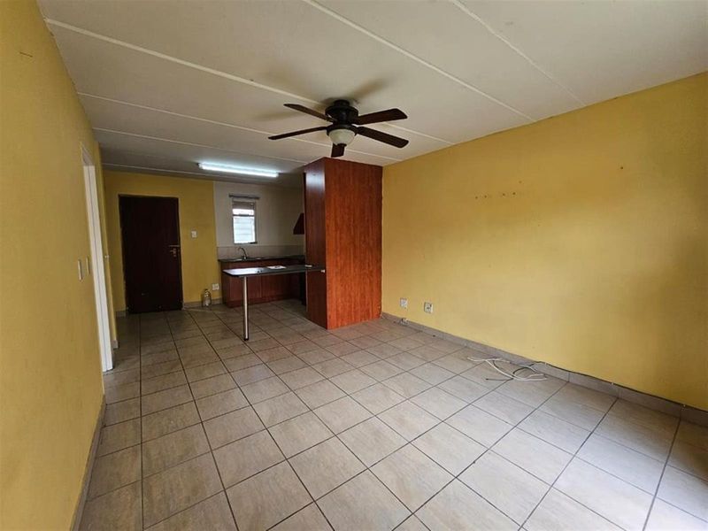 An open-plan living and kitchen area featuring tiled flooring, a ceiling fan, and basic kitchen cabinetry with a breakfast counter.