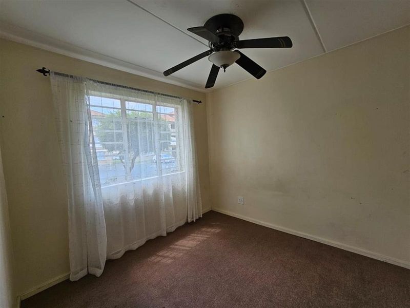 An empty bedroom featuring a ceiling fan, carpeted flooring, and a window with natural light.