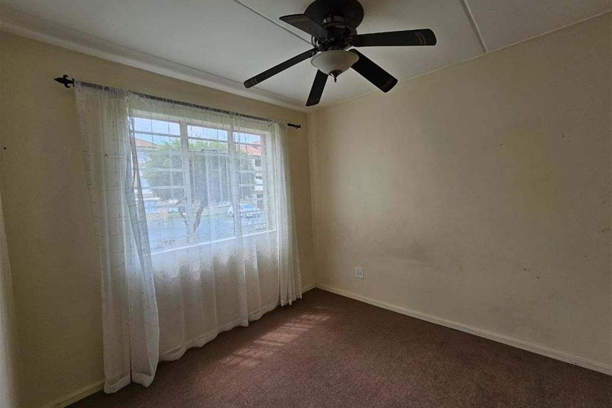 An empty bedroom featuring a ceiling fan, carpeted flooring, and a window with natural light.