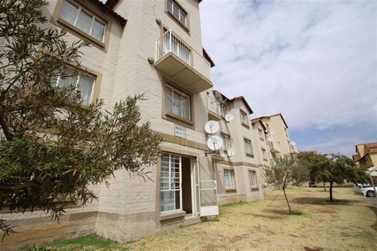 Exterior view of a multi-story townhouse complex featuring brick facades, private balconies, and communal garden space.