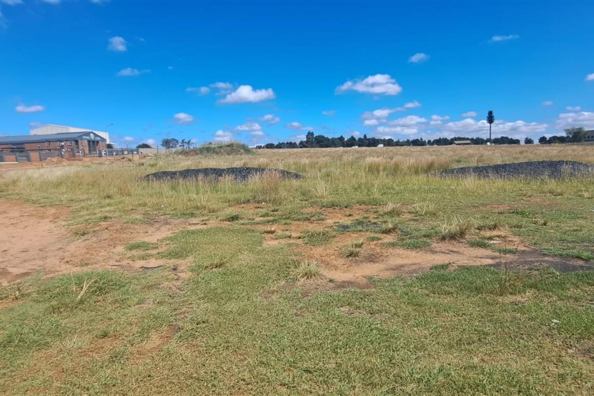 A wide-angle view of a vacant agricultural land plot featuring open grass fields and surrounding industrial infrastructure.