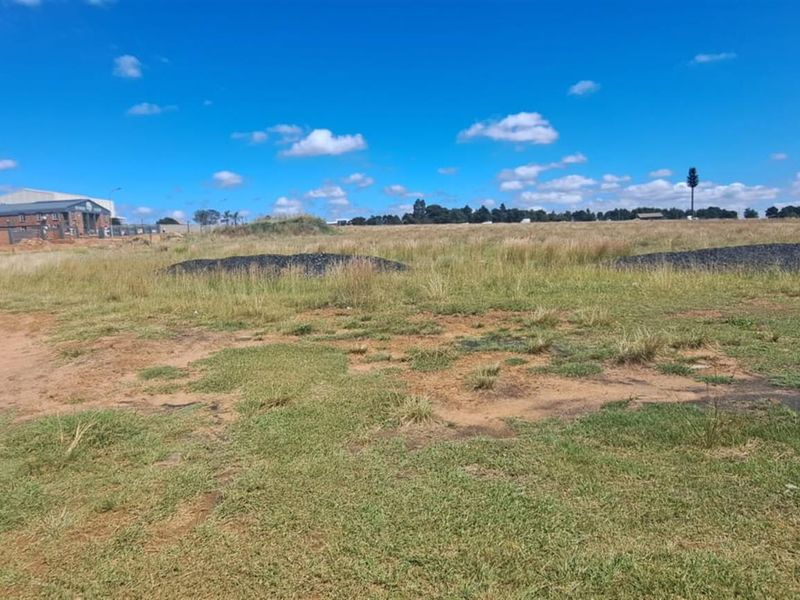 A wide-angle view of a vacant agricultural land plot featuring open grass fields and surrounding industrial infrastructure.