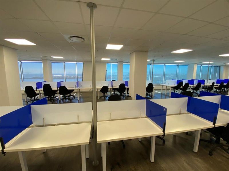 Open-plan office space featuring large floor-to-ceiling windows with panoramic views, suspended ceiling tiles, and integrated desk partitions.